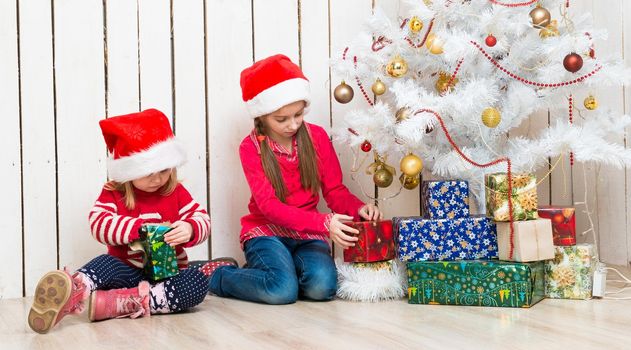 two little girls open christmas presents sitting on the floor near decorated new year tree