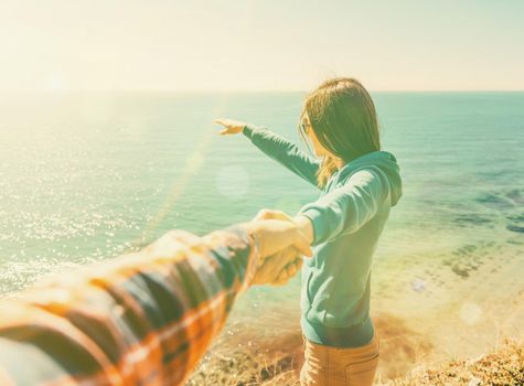Couple in love. Beautiful young woman holding man's hand and showing him something in distance the sea. Image with sunlight effect. Point of view shot