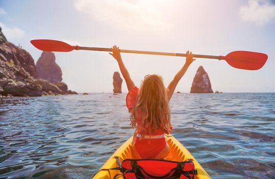 Young brunette woman in red swimsuit and Santa hat, swimming on kayak around basalt rocks like in Iceland. Back view. Christmas and travel concept