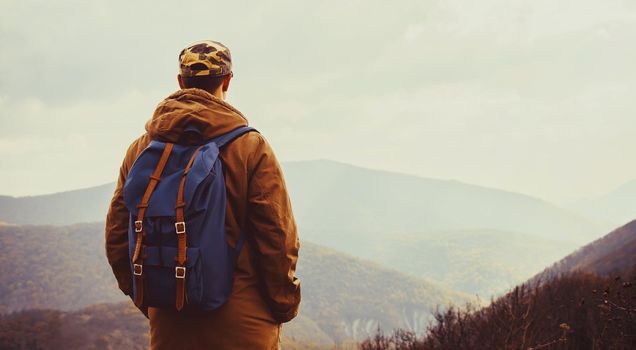 Hiker young man with backpack enjoying view of mountains, rear view