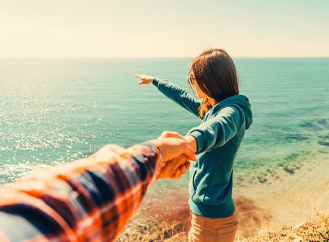 Couple in love. Beautiful young woman holding man's hand and showing him something in distance the sea. Point of view shot. Image with instagram filter