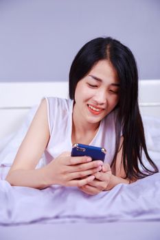 happy woman using a phone in her hand on bed in the bedroom