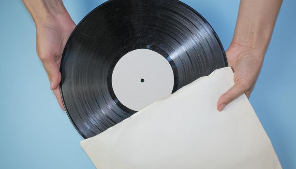 Hands hold an old vinyl record in an old paper case on a light blue background