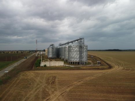 Grain elevator. Metal grain elevator in agricultural zone. Agriculture storage for harvest. Grain elevators on green nature background. Exterior of agricultural factory