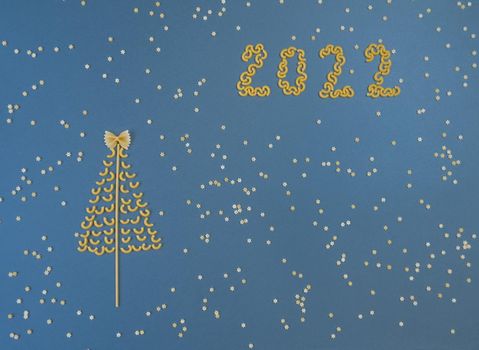 Christmas tree lined with dry pasta and numbers 2022 and stars from pasta on a blue paper background