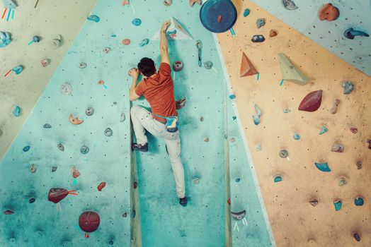 Free climber young man climbing artificial boulder indoors