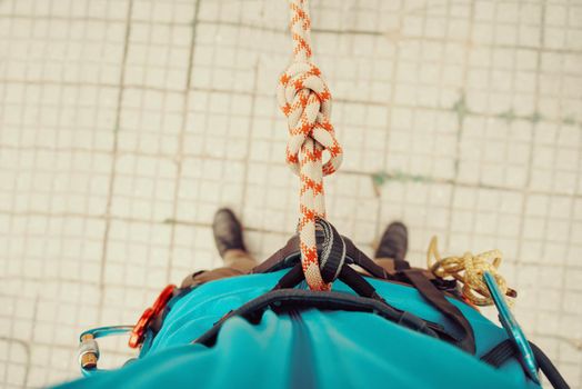 Climber man standing in harness with rope and knot Eight. Point of view shot. Top view