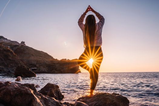 Young woman in swimsuit with long hair practicing stretching outdoors on yoga mat by the sea on a sunny day. Women's yoga fitness pilates routine. Healthy lifestyle, harmony and meditation concept.