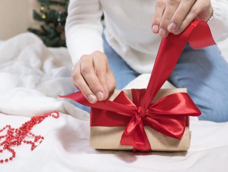 Happy Holidays. Female hands untie a bow on a gift box for Christmas in a white bed