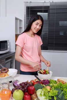 young woman mixing salad while cooking in kitchen 