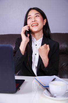 Cheerful young business woman sitting at the desk and talking on mobile phone