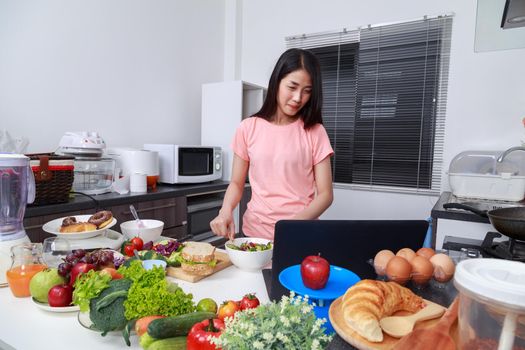 young woman mixing salad while cooking with laptop in kitchen 