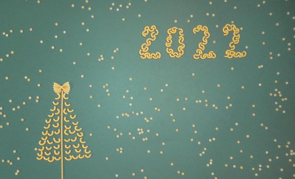 Christmas tree lined with dry pasta and numbers 2022 and stars from pasta on a green paper background