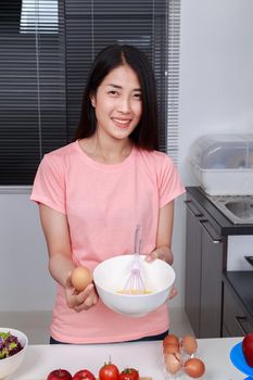 woman cooking and whisking eggs in a bowl in kitchen room