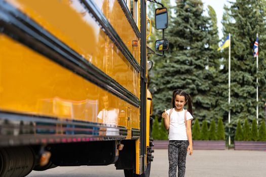 Cute girl with a backpack standing near bus going to school posing to camera pensive close-up