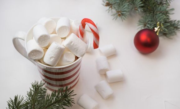 hot chocolate with marshmallows in a red and white bakery on a white background and branches of a New Year tree