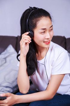 young woman listening to music in headphones with moblie on sofa at home