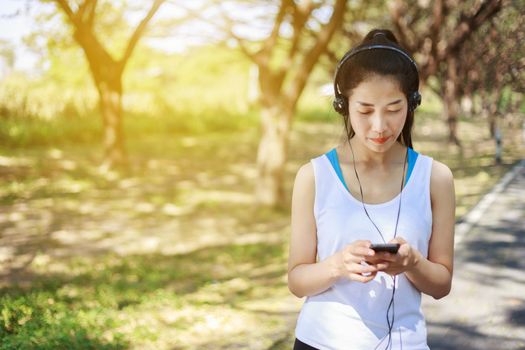 young sporty woman using smartphone with headphone in the park