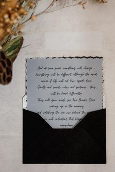 wedding invitation in a gray envelope on a table with green sprigs