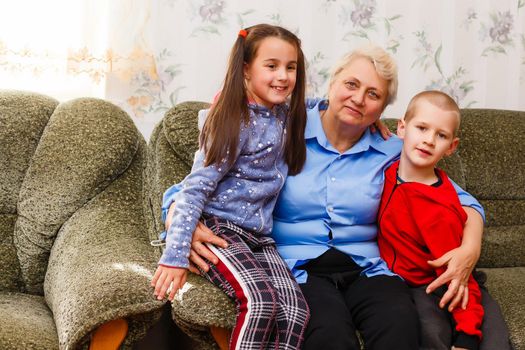 Closeup portrait of happy great-grandmother with great-grandchildren on the sofa at home