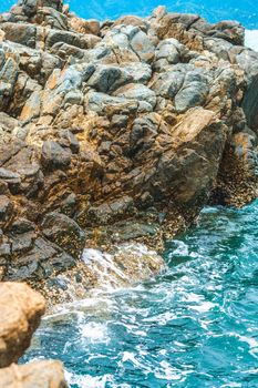 Beautiful natural composition landmark background. Bright vivid brown gray stone rock shabby cliff cracks texture mountains, lazur sea water splash. Concept of geology, tourism cruise, power nature