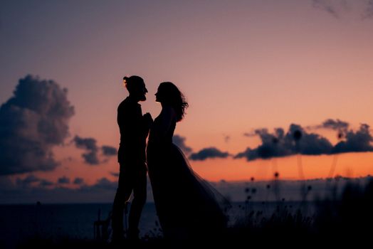silhouettes of a happy young couple guy and girl on a background of orange sunset in the ocean