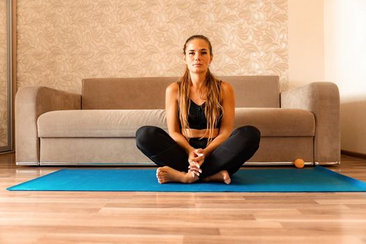 Young woman with long hair, fitness instructor in black sportswear, doing stretching and pilates on yoga mat at home. Female fitness yoga routine concept. Healthy lifestyle harmony and meditation