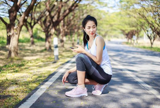 young sporty woman sitting on the road in the park and using smartphone with earphone to listening music