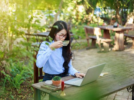 young woman drinking coffee and working with laptop in the garden