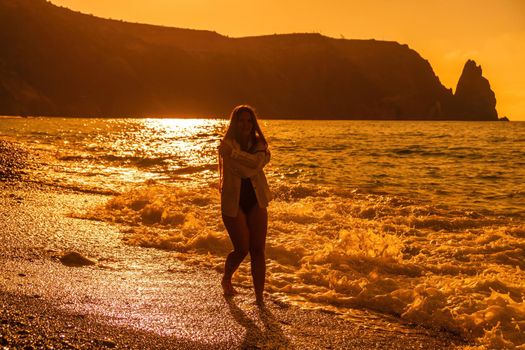 Selective focus. Happy carefree sensual woman with long hair in black swimwear posing at sunset beach. Silhouette of young beautiful playful positive woman outdoor. Summer vacation and trip concept.