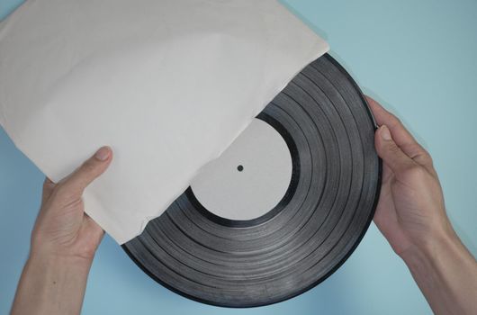 Hands hold an old vinyl record in an old paper case on a light blue background