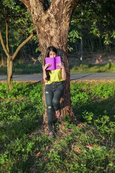 young woman stading at the tree and reading a book in the park