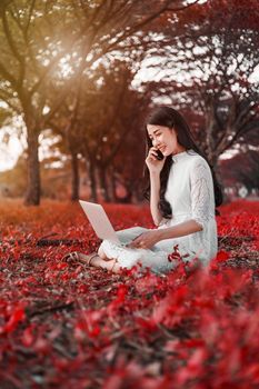 beautiful woman using laptop and calling with mobile phone in the outdoor park