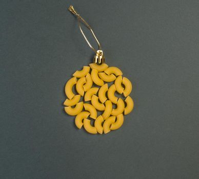 Christmas decoration on a tree in the form of a ball of pasta on a dark gray paper background, top view. Conceptual photo