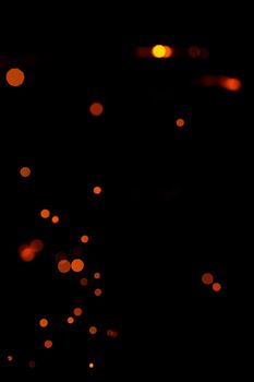 Orange bokeh on a black background, burning and blurred sparks from the fire. Particles of burning embers fly and glow isolated in the night sky 2021.