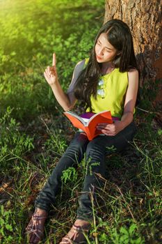 young woman thinking and holding a book in the park