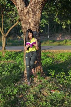 young woman stading at the tree and reading a book in the park