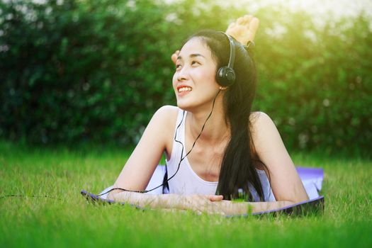 young woman listening to music with headphones and laying on a grass field