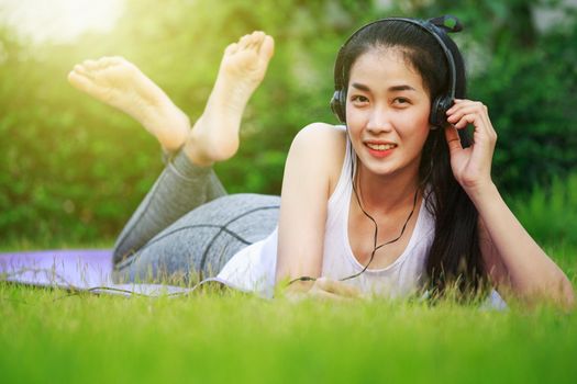 young woman listening to music with headphones and laying on a grass field