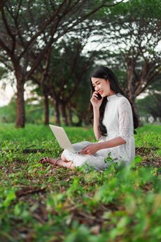 beautiful woman using laptop and calling with mobile phone in the outdoor park