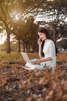 beautiful woman using laptop and calling with mobile phone in the outdoor park