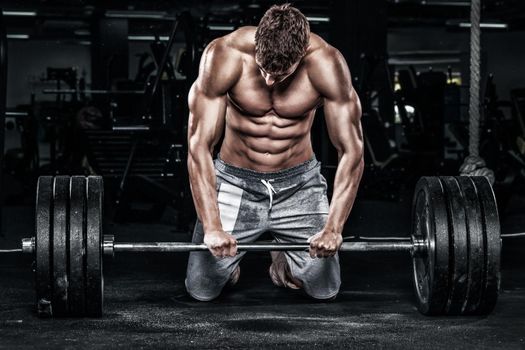 Athletic shirtless young sports man - fitness model with barbell in gym.