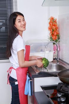 Woman washing broccoli under running water at the kitchen sink at home