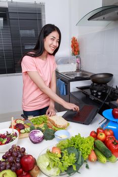 young happy woman cooking and looking with laptop in kitchen room