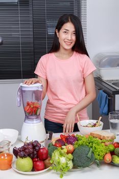 young woman making smoothies with blender in kitchen