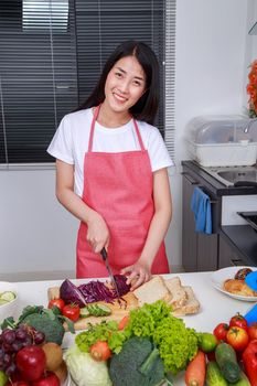 woman cutting purple cabbage on board in kitchen room at home