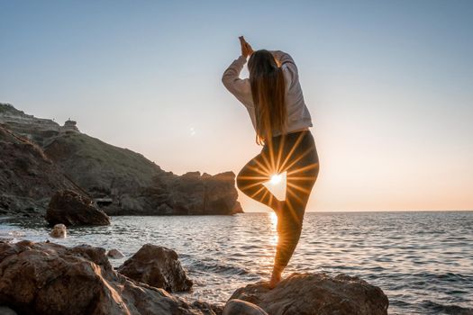 Young woman in swimsuit with long hair practicing stretching outdoors on yoga mat by the sea on a sunny day. Women's yoga fitness pilates routine. Healthy lifestyle, harmony and meditation concept.