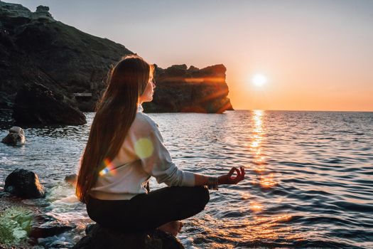 Young woman in swimsuit with long hair practicing stretching outdoors on yoga mat by the sea on a sunny day. Women's yoga fitness pilates routine. Healthy lifestyle, harmony and meditation concept.