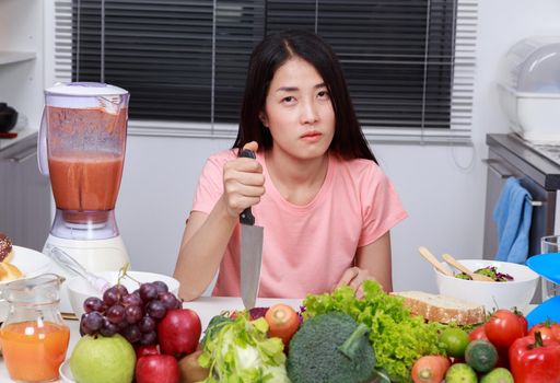 depressed young woman cooking with knife in kitchen room