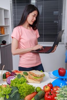 young woman cooking and looking with laptop in kitchen room